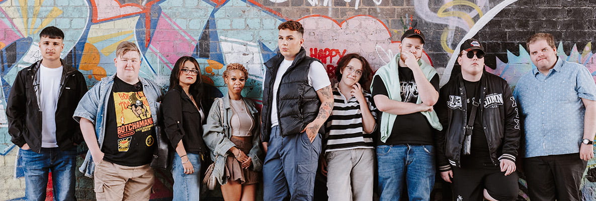 An image of youth standing in front of a graffiti wall