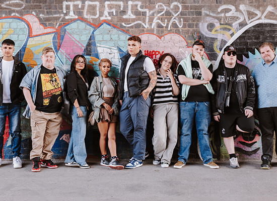 An image of youth standing in front of a graffiti wall